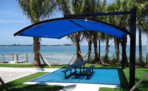 Curved square shade structure over park bench on waterfront.