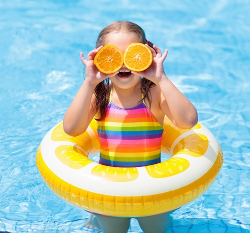 a kid on a swimming pool covering her eyes with oranges