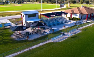 Square shade structure over bleachers and umbrella-shaped shade structures over tables at sports field.